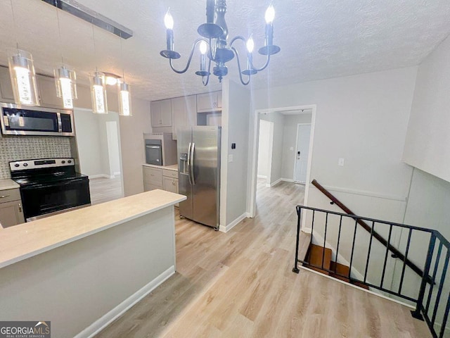 kitchen featuring tasteful backsplash, a textured ceiling, stainless steel appliances, decorative light fixtures, and light hardwood / wood-style flooring