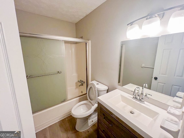 full bathroom with a textured ceiling, hardwood / wood-style flooring, shower / bath combination with glass door, toilet, and vanity