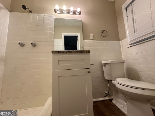 bathroom with toilet, tile walls, tiled shower, and hardwood / wood-style floors