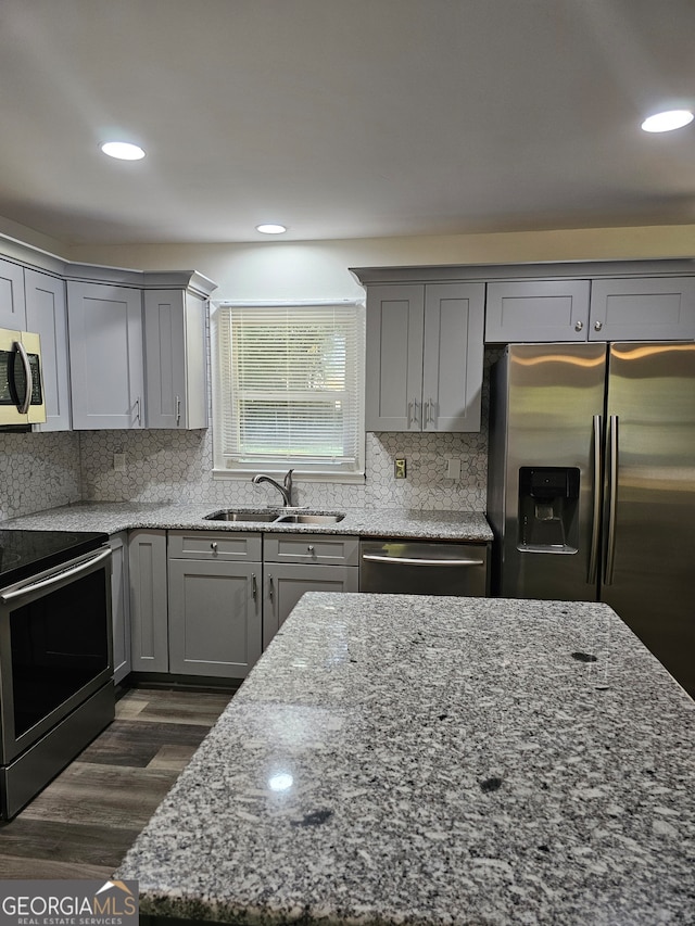 kitchen with light stone counters, backsplash, appliances with stainless steel finishes, dark hardwood / wood-style flooring, and sink