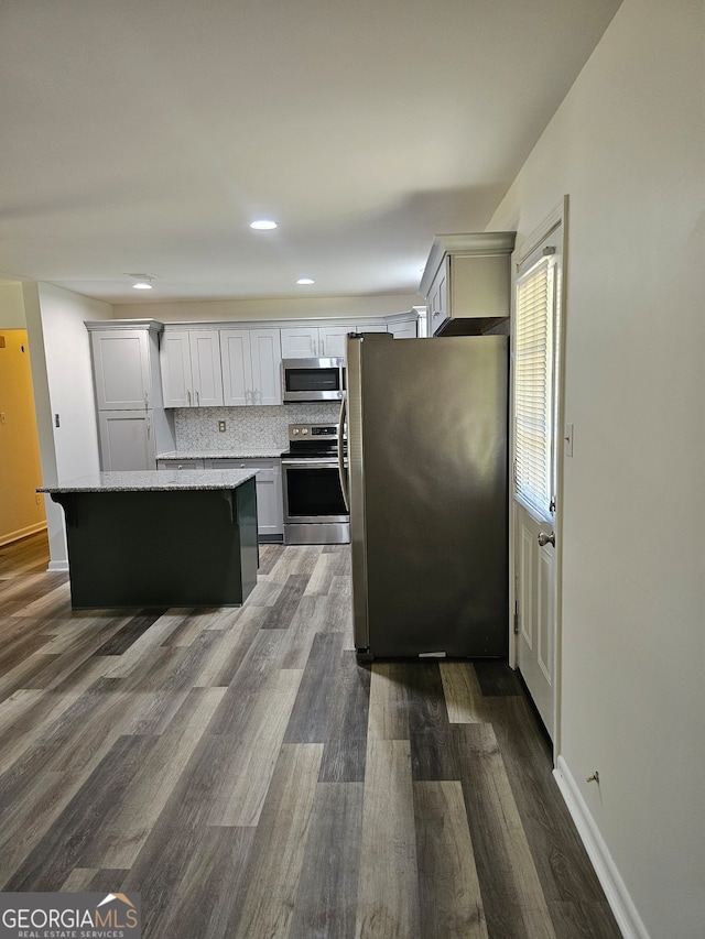 kitchen with tasteful backsplash, appliances with stainless steel finishes, a kitchen island, dark wood-type flooring, and light stone counters