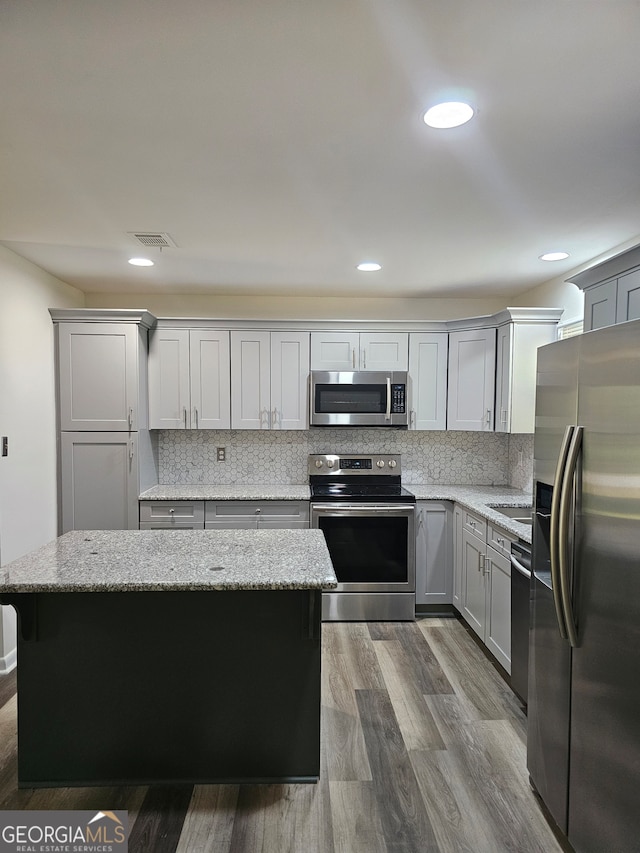 kitchen with stainless steel appliances, decorative backsplash, a center island, and hardwood / wood-style floors