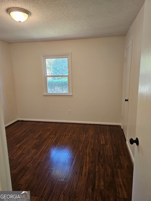 unfurnished room featuring a textured ceiling and dark hardwood / wood-style flooring