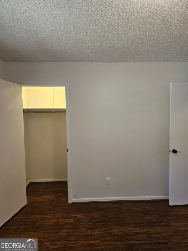 unfurnished bedroom featuring a closet, a textured ceiling, dark hardwood / wood-style flooring, and a spacious closet