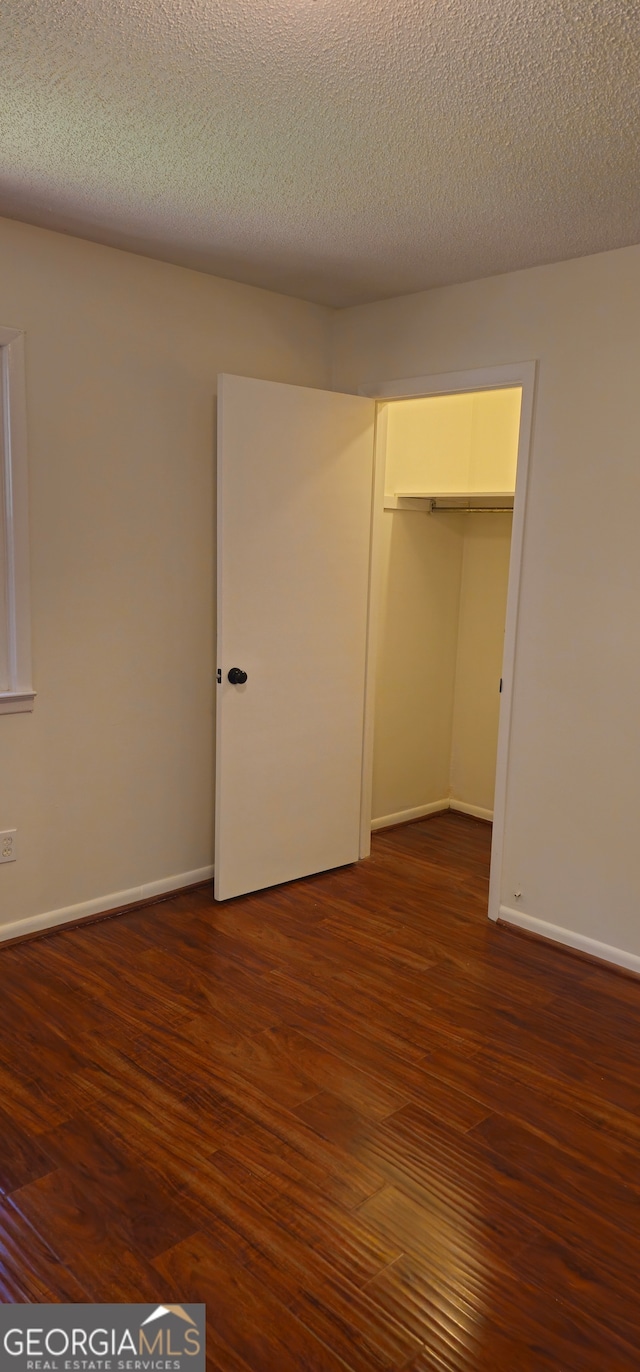 unfurnished bedroom with a closet, a textured ceiling, a spacious closet, and dark hardwood / wood-style floors