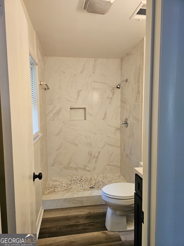 bathroom with toilet, a tile shower, vanity, and wood-type flooring