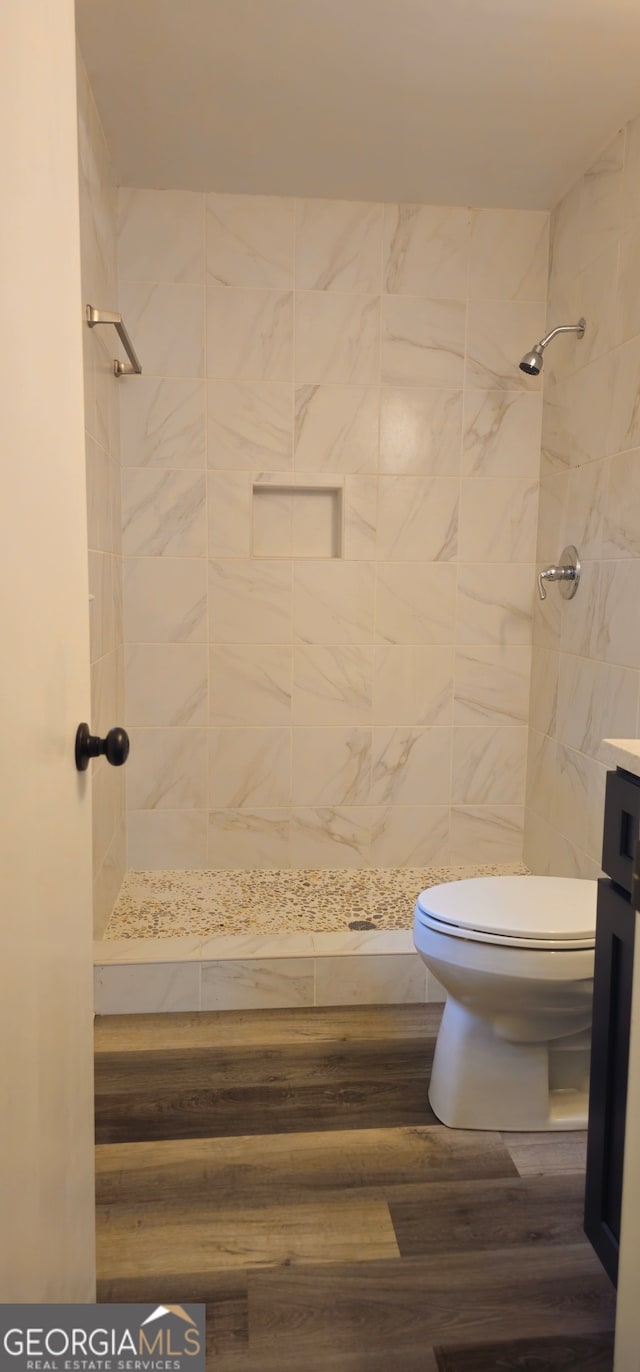 bathroom with toilet, hardwood / wood-style floors, vanity, and tiled shower