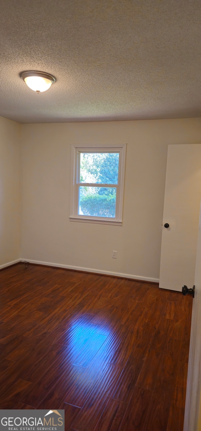 empty room featuring a textured ceiling and dark hardwood / wood-style floors