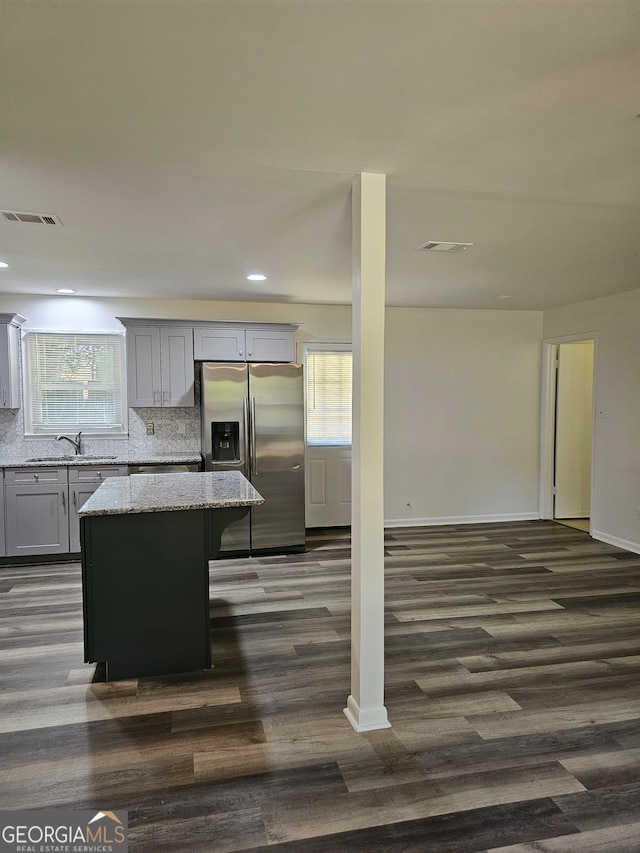 kitchen featuring light stone countertops, sink, a kitchen island, dark wood-type flooring, and stainless steel refrigerator with ice dispenser