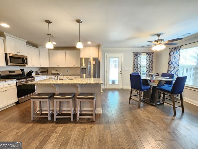 kitchen with hanging light fixtures, a center island with sink, white cabinetry, appliances with stainless steel finishes, and dark hardwood / wood-style flooring