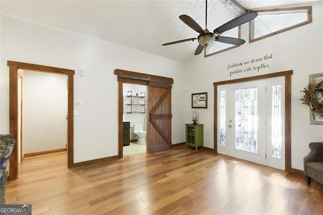 foyer entrance featuring a barn door, light hardwood / wood-style flooring, ceiling fan, and lofted ceiling