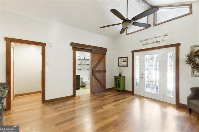 foyer with a barn door, vaulted ceiling, a ceiling fan, light wood-style floors, and baseboards
