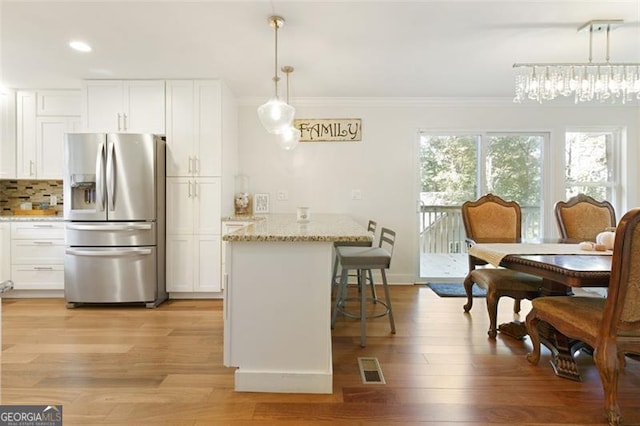 kitchen with a kitchen bar, light stone countertops, decorative light fixtures, white cabinets, and stainless steel fridge with ice dispenser