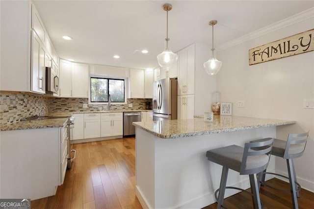 kitchen featuring light wood finished floors, stainless steel appliances, light stone countertops, decorative backsplash, and a peninsula