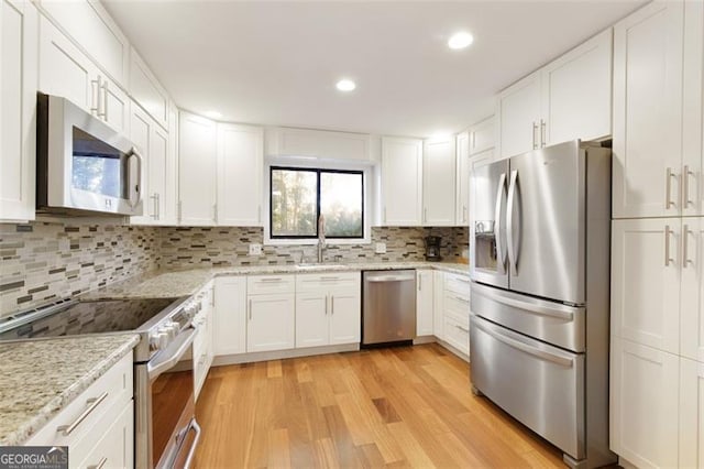 kitchen featuring light wood-type flooring, stainless steel appliances, white cabinetry, and tasteful backsplash