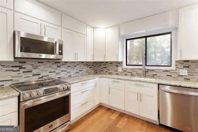 kitchen featuring white cabinets, a sink, decorative backsplash, light wood-style flooring, and appliances with stainless steel finishes