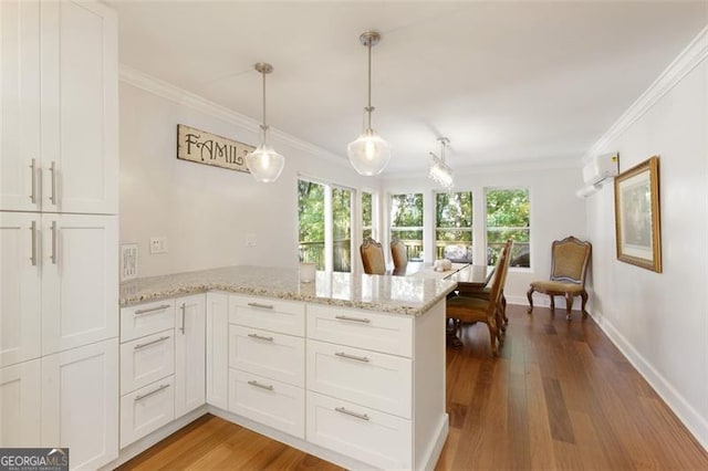 kitchen featuring kitchen peninsula, wood-type flooring, decorative light fixtures, and white cabinetry