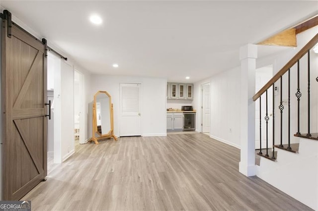 unfurnished living room with a barn door, light wood finished floors, baseboards, wine cooler, and recessed lighting