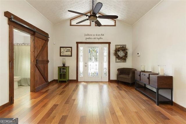foyer entrance with a barn door, a ceiling fan, light wood finished floors, lofted ceiling, and ornamental molding