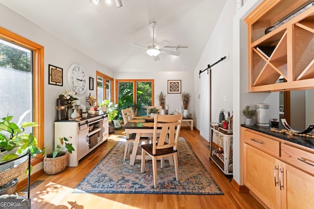 dining room with vaulted ceiling, a barn door, light hardwood / wood-style flooring, and ceiling fan