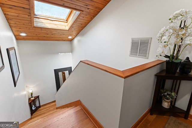 stairway with vaulted ceiling with skylight, wood ceiling, and wood-type flooring