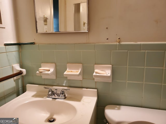 bathroom with toilet, vanity, and tile walls