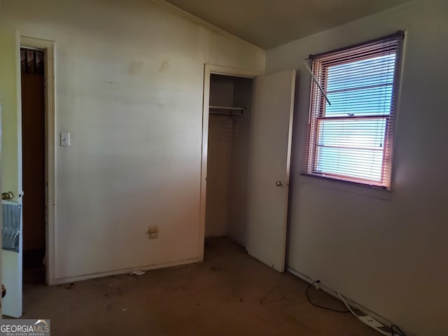 unfurnished bedroom with a closet, ornamental molding, vaulted ceiling, and light colored carpet