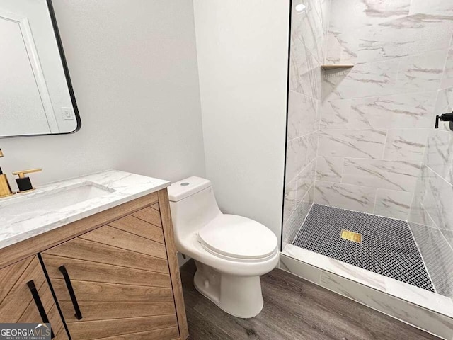 bathroom featuring vanity, hardwood / wood-style floors, a tile shower, and toilet