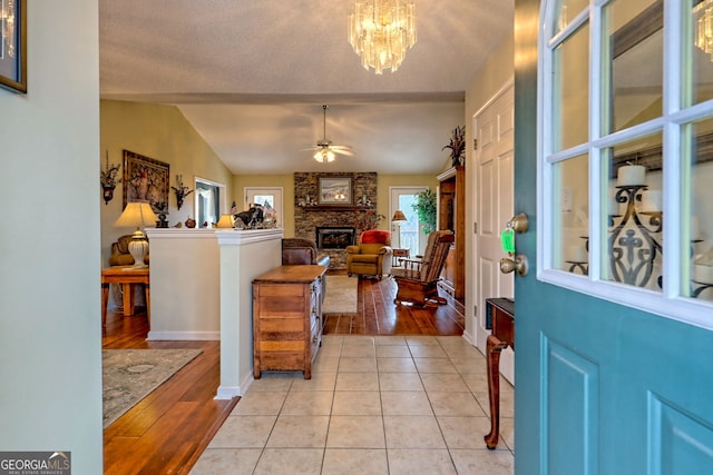 tiled entrance foyer featuring lofted ceiling, a stone fireplace, and ceiling fan with notable chandelier