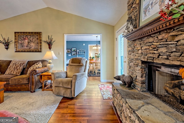 living room featuring dark hardwood / wood-style flooring, a chandelier, vaulted ceiling, and a stone fireplace