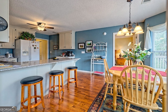 kitchen featuring hardwood / wood-style floors, ceiling fan with notable chandelier, white cabinetry, hanging light fixtures, and white refrigerator with ice dispenser