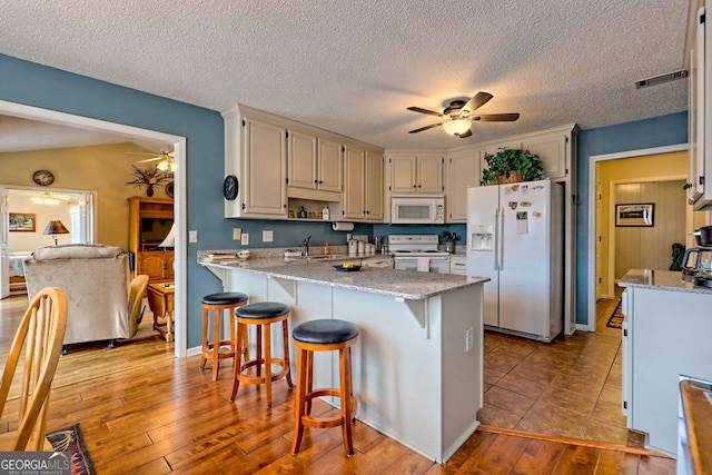 kitchen featuring sink, a kitchen bar, ceiling fan, white appliances, and light hardwood / wood-style flooring