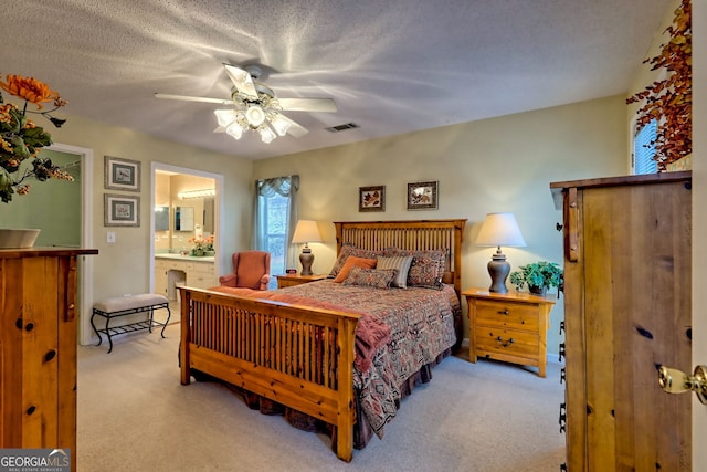 bedroom with ceiling fan, light colored carpet, a textured ceiling, and ensuite bathroom