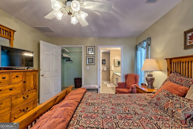 bedroom with ceiling fan, ensuite bathroom, a textured ceiling, a walk in closet, and a closet