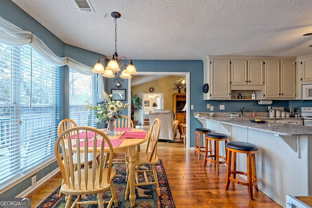 dining room featuring an inviting chandelier, sink, light hardwood / wood-style flooring, and a textured ceiling