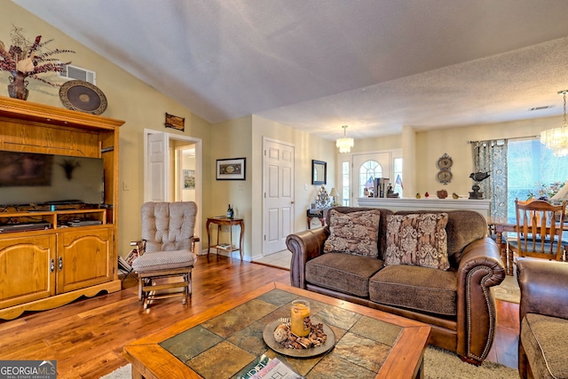 living room featuring vaulted ceiling, wood-type flooring, a textured ceiling, and a chandelier