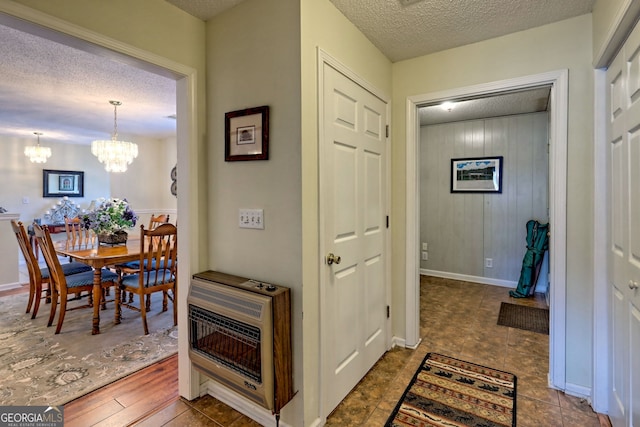 hallway with an inviting chandelier, heating unit, and a textured ceiling