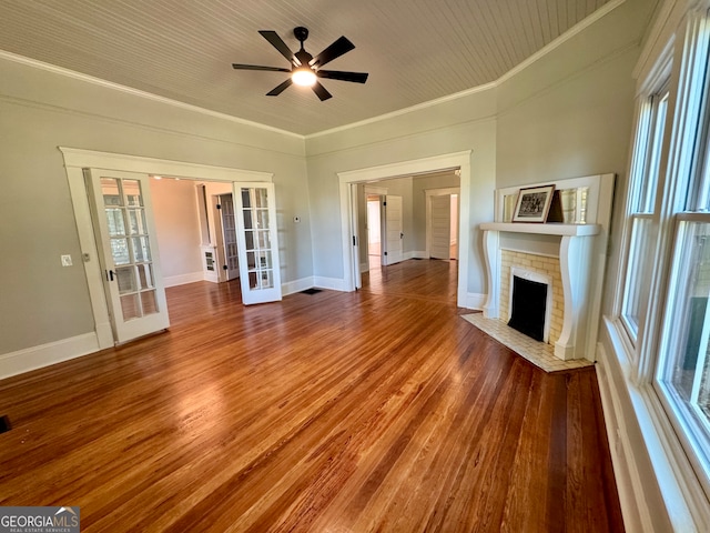 unfurnished living room with ceiling fan, hardwood / wood-style flooring, ornamental molding, a fireplace, and french doors