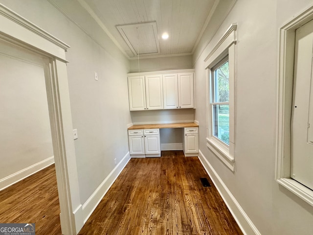 unfurnished office featuring built in desk, ornamental molding, and dark hardwood / wood-style floors