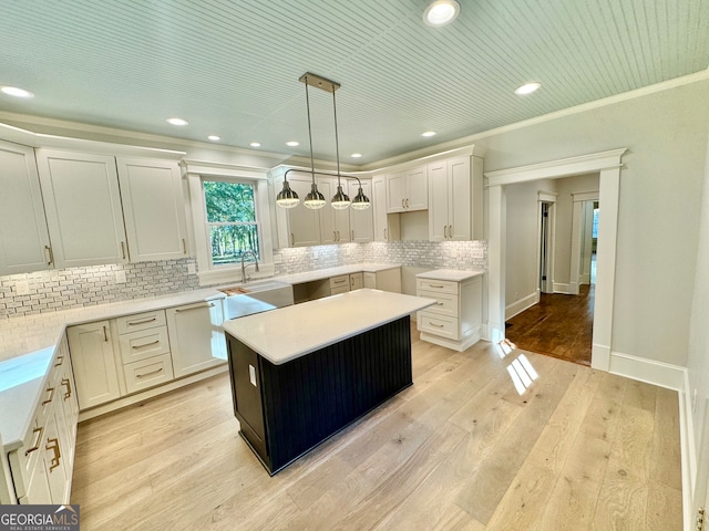 kitchen featuring white cabinetry, a center island, ornamental molding, light hardwood / wood-style floors, and decorative light fixtures