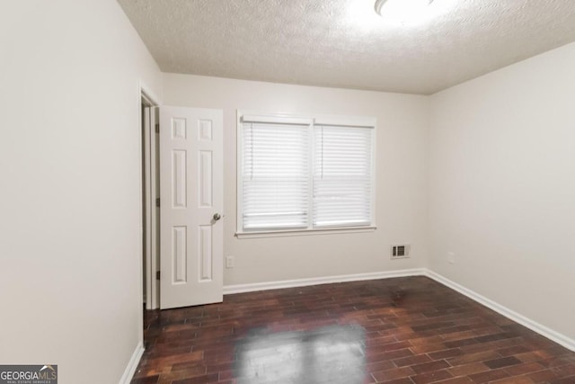 empty room featuring a textured ceiling and dark hardwood / wood-style floors