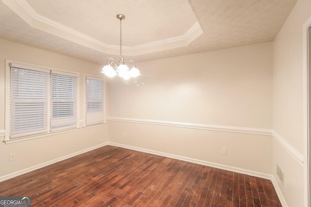 empty room featuring dark wood-type flooring, a raised ceiling, a textured ceiling, and an inviting chandelier