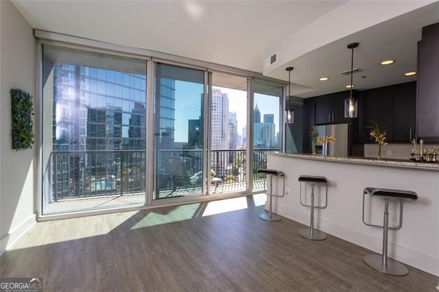 kitchen with light stone counters, a kitchen bar, dark hardwood / wood-style flooring, stainless steel refrigerator with ice dispenser, and floor to ceiling windows