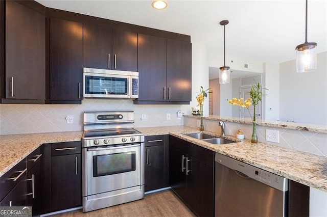 kitchen featuring stainless steel appliances, sink, tasteful backsplash, decorative light fixtures, and light hardwood / wood-style flooring