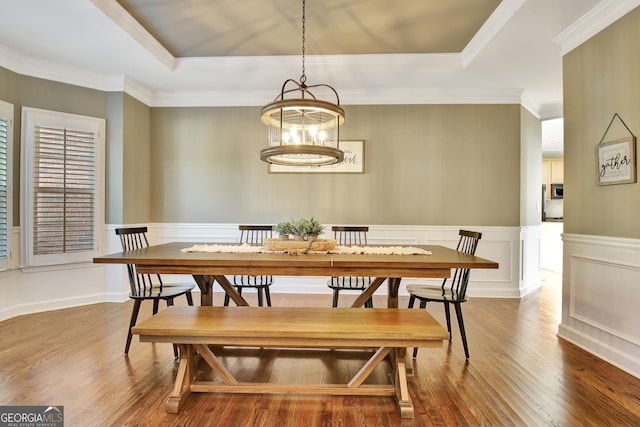 dining area featuring an inviting chandelier, hardwood / wood-style flooring, a raised ceiling, and crown molding