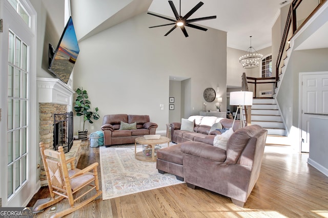 living room with ceiling fan with notable chandelier, a fireplace, a high ceiling, and light hardwood / wood-style flooring