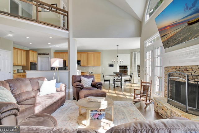 living room featuring light wood-type flooring, high vaulted ceiling, a stone fireplace, and a notable chandelier