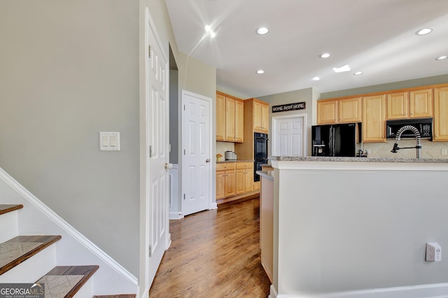 kitchen with black appliances, hardwood / wood-style flooring, light brown cabinetry, and tasteful backsplash