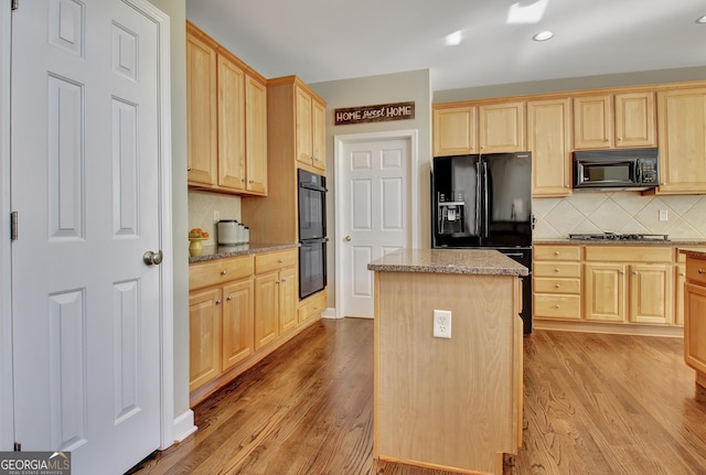 kitchen with a center island, backsplash, black appliances, light wood-type flooring, and light stone counters