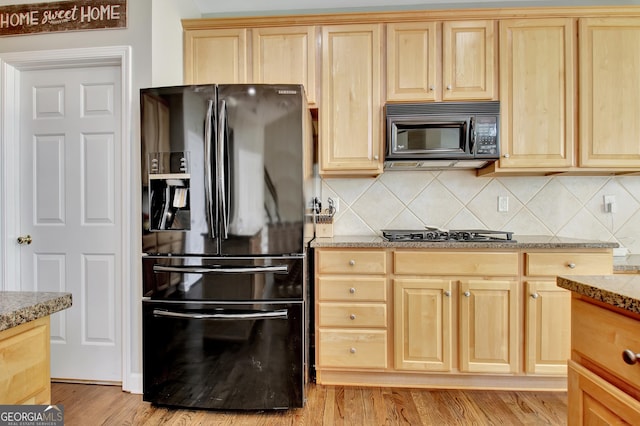 kitchen with tasteful backsplash, light stone countertops, light hardwood / wood-style flooring, and black appliances